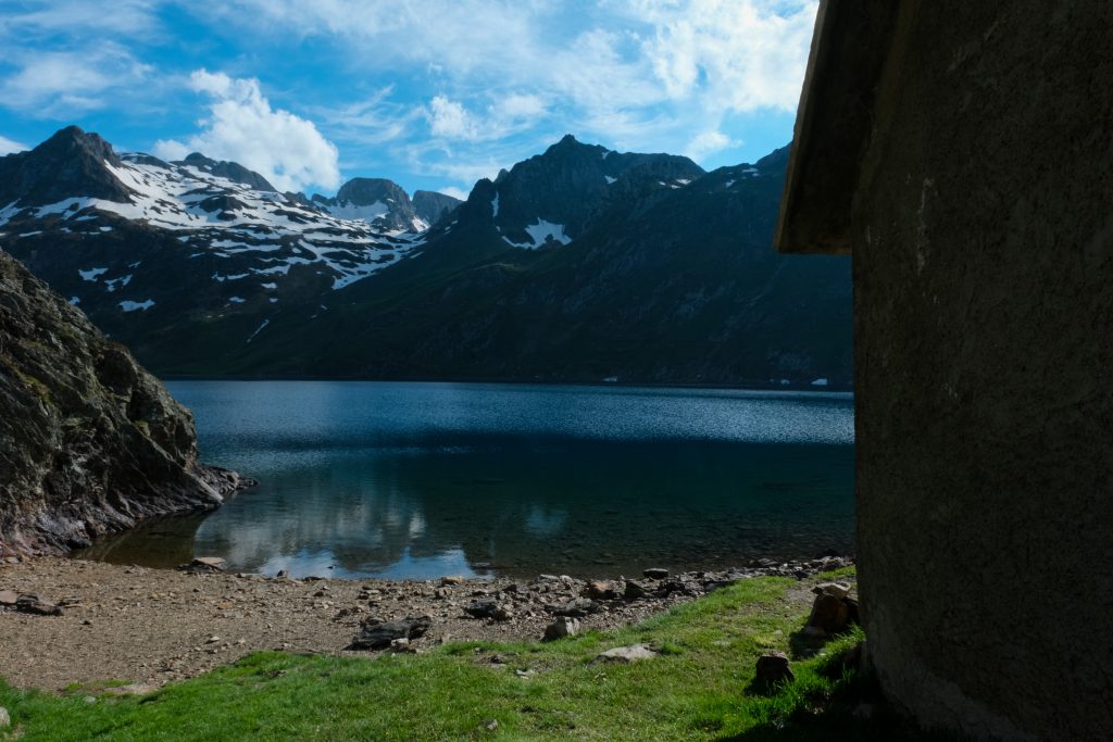 Photo du lac bleu avec un peu de verdure devant et une cabane sur la droite